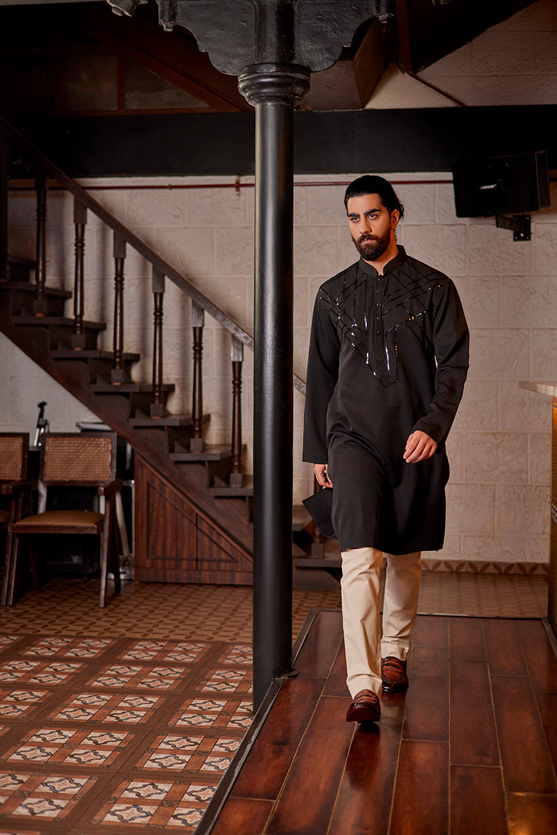 A man in a black lycra silk kurta from BenzerWorld ethnicwear store poses in front of a pole.