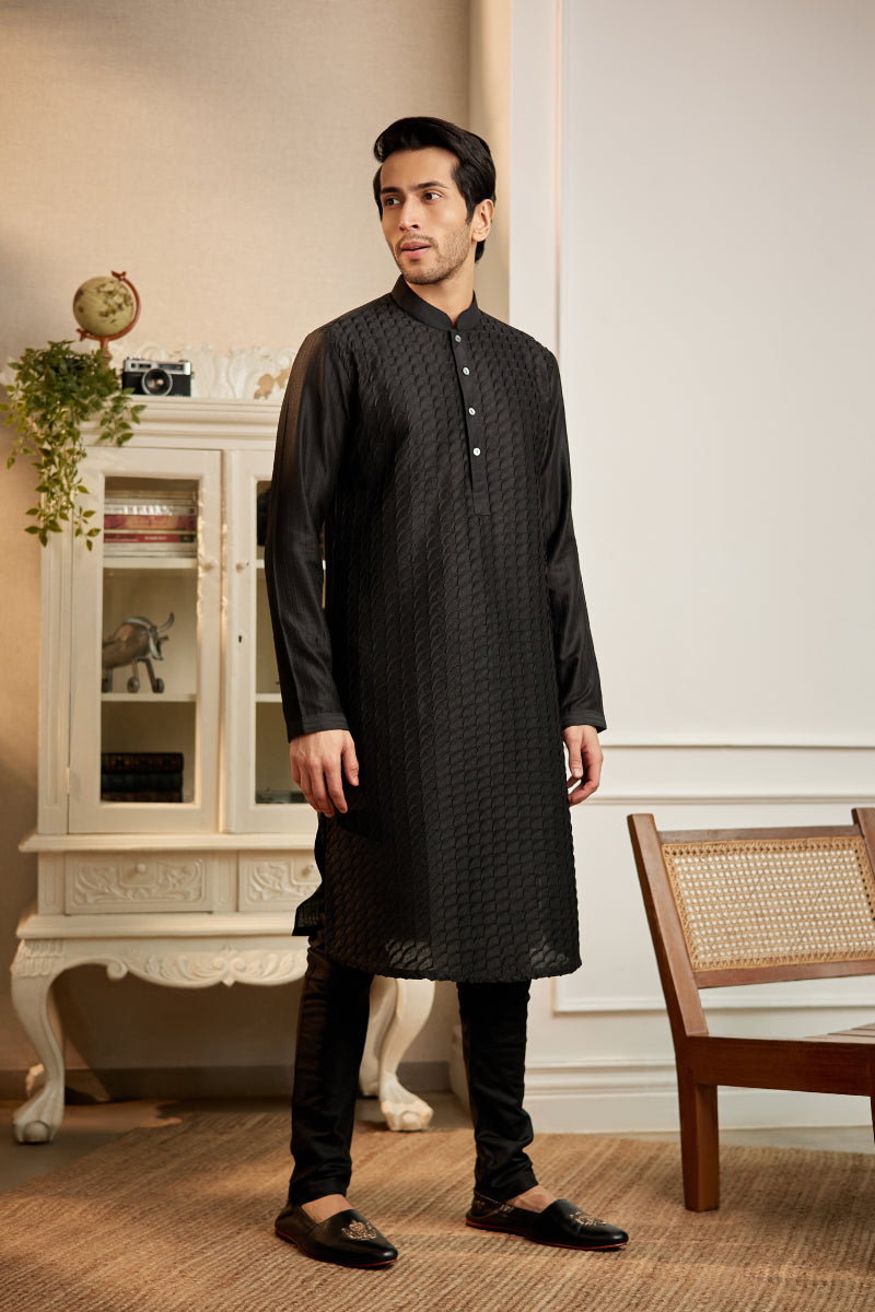 A man in a black cotton silk kurta set from BenzerWorld ethnicwear store poses in a standing position, with legs apart.