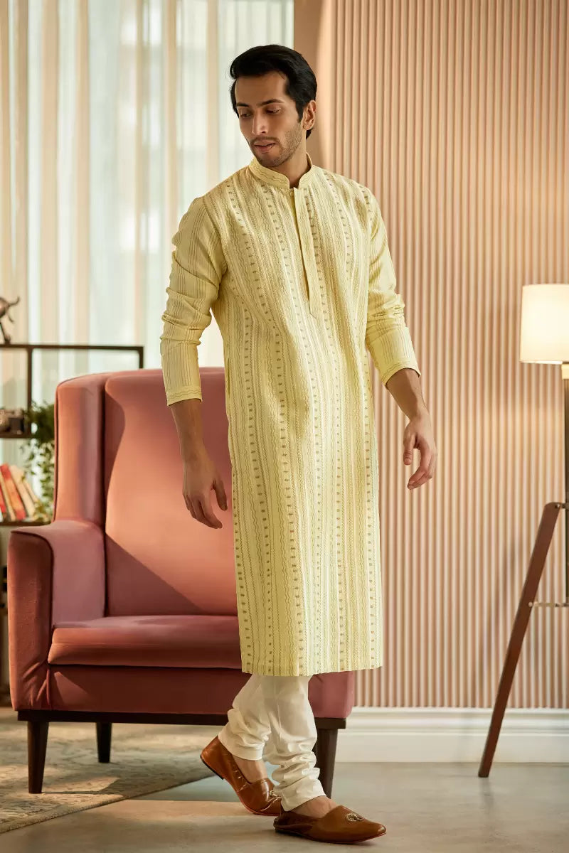 A man in a light yellow chanderi silk kurta set from BenzerWorld ethnicwear store poses for the camera.