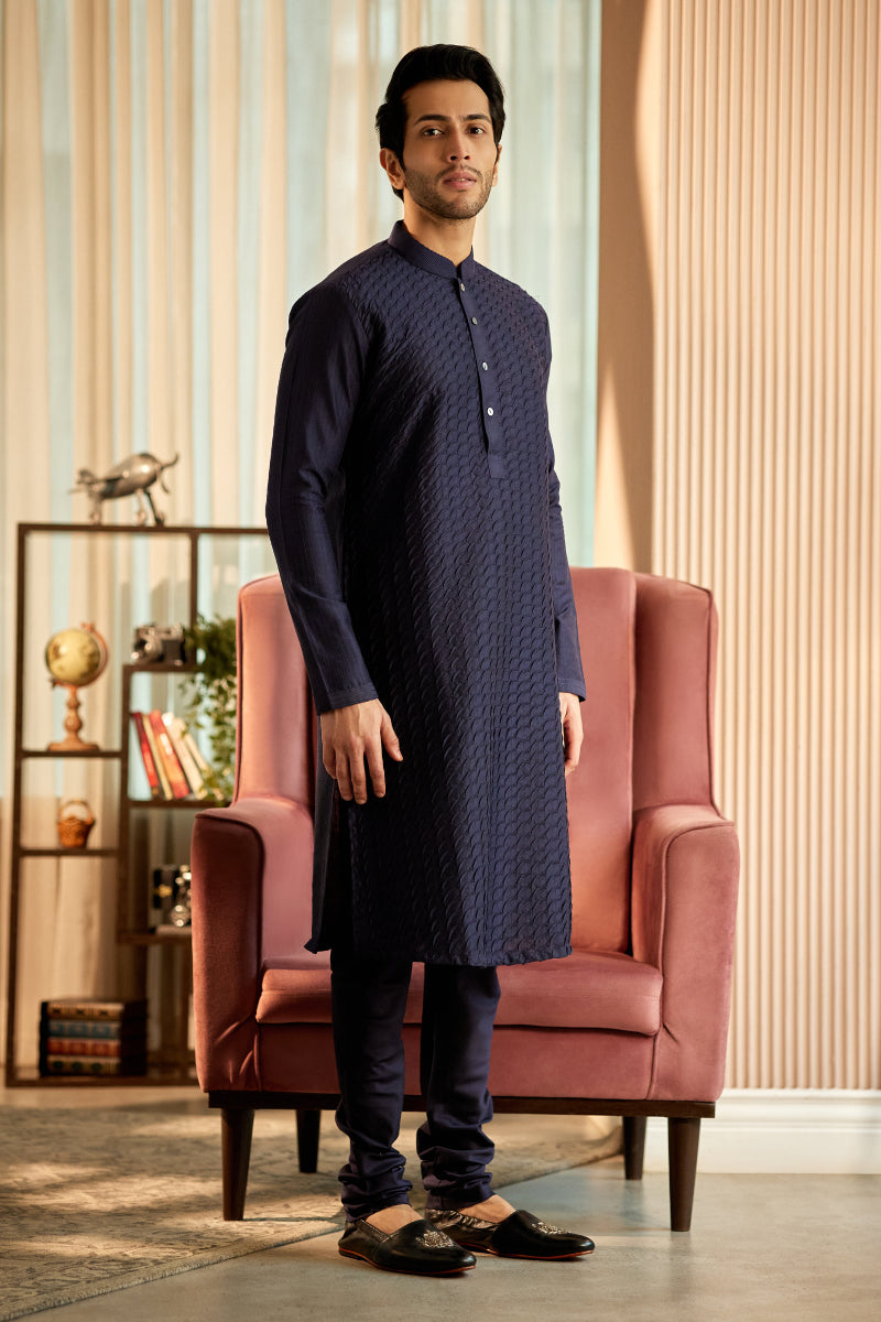 A man in a navy blue cotton silk kurta set from BenzerWorld ethnicwear store poses in a sitting position.